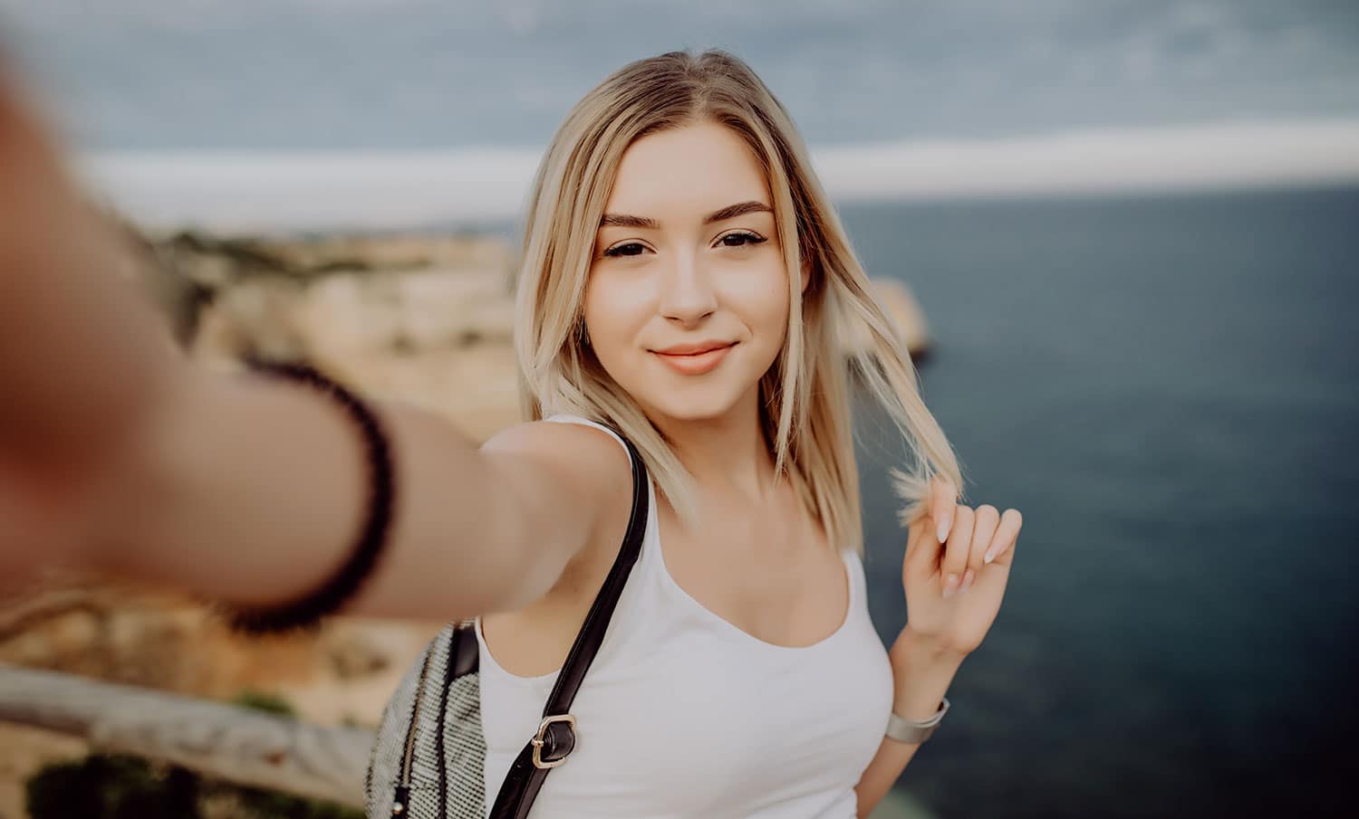 Beautiful young woman doing selfie on the cliff